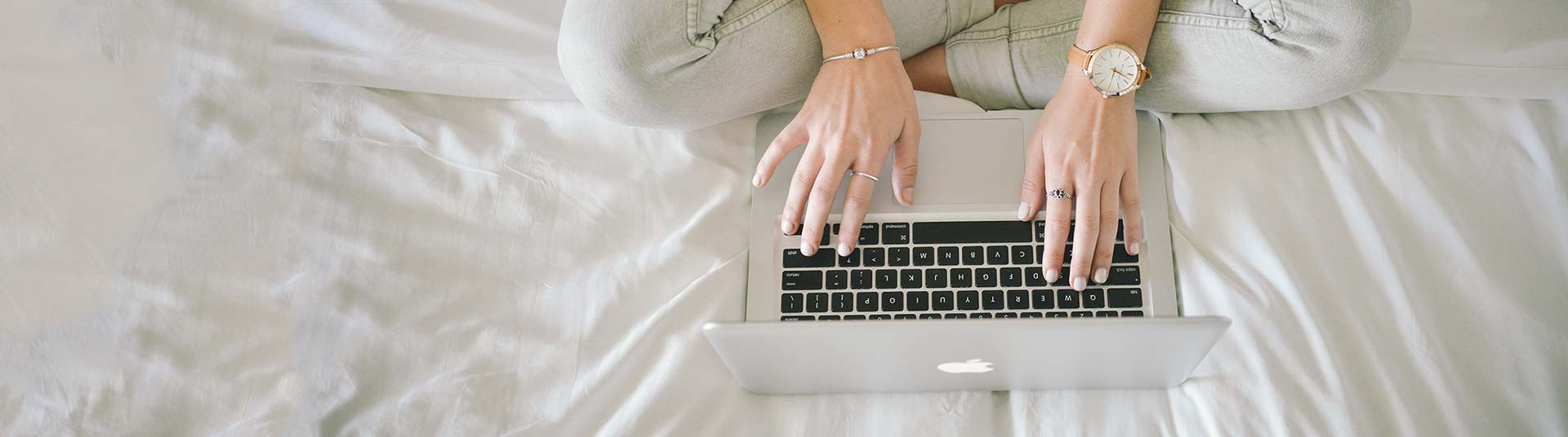 A woman sitting on her bed typing on her laptop